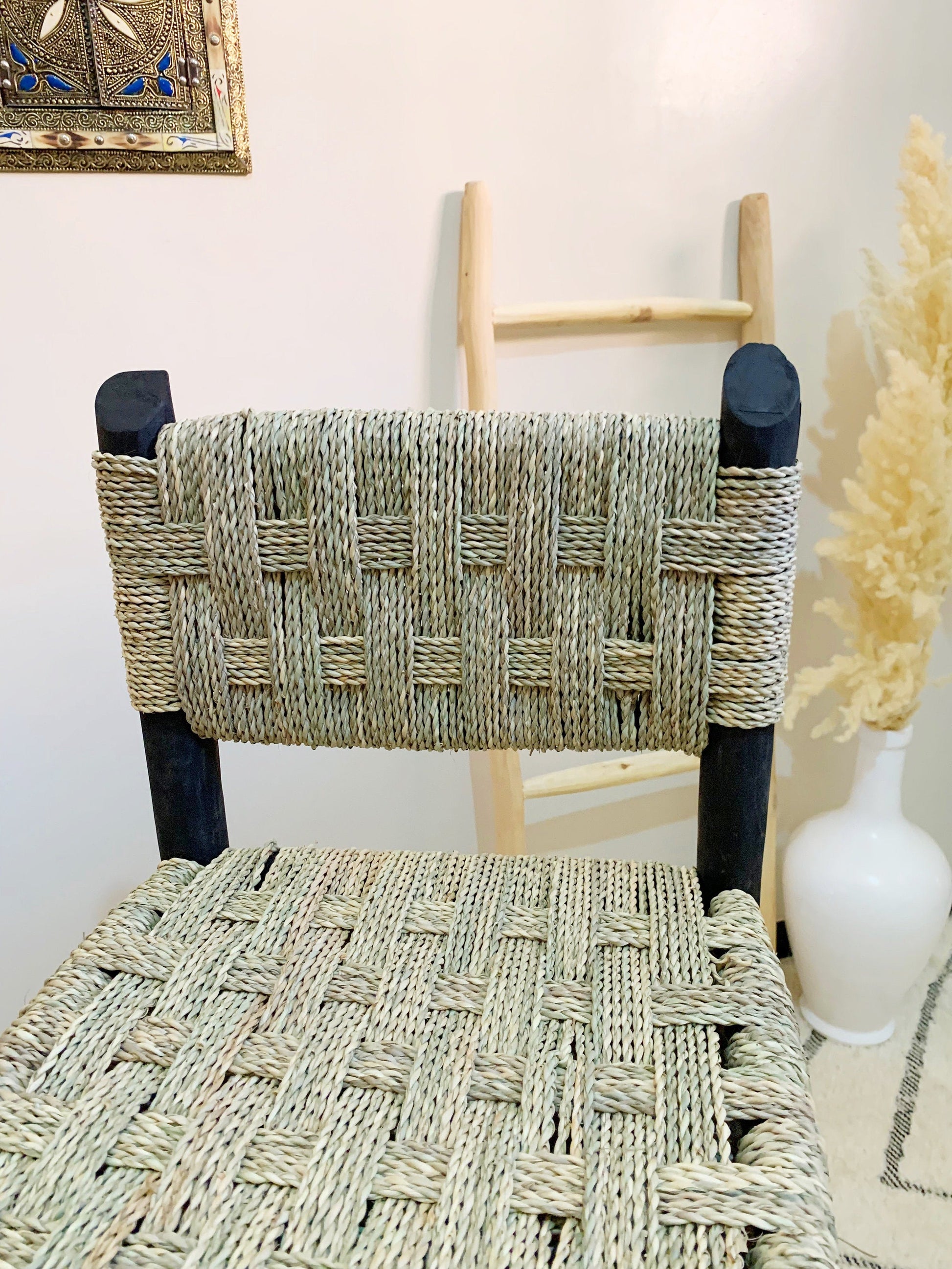 a wicker chair next to a vase with a plant in it